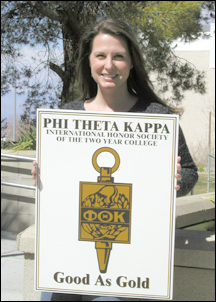 Christine Swiridoff holding a sign showing the emblem of the Phi Theta Kappa honors society.